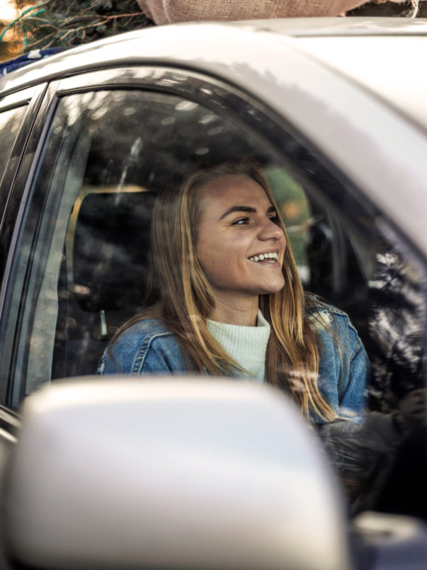 Kvinne sitter i passasjersetet av en bil og smiler.
